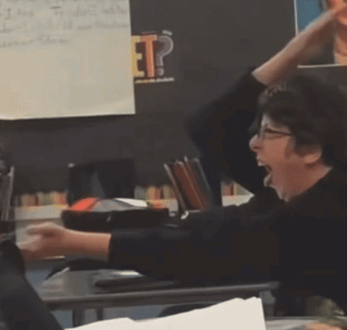 A Woman Sitting At A Desk With Her Hands In The Air In Front Of A Blackboard With The Word Ep On It GIF