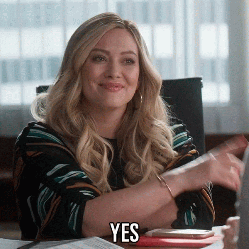 A Woman Sitting At A Desk With The Word Yes On Her Chest GIF