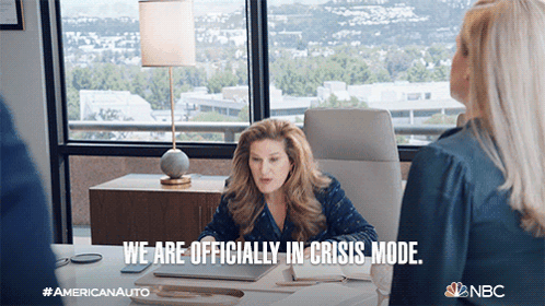 a woman sitting at a desk with the words we are officially in crisis mode below her