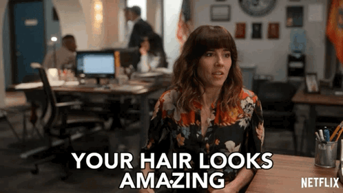 A Woman Sitting At A Desk With The Words " Your Hair Looks Amazing " On The Screen GIF