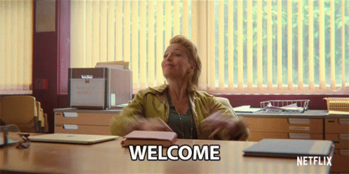 A Woman Sitting At A Desk With Welcome Written On The Table GIF