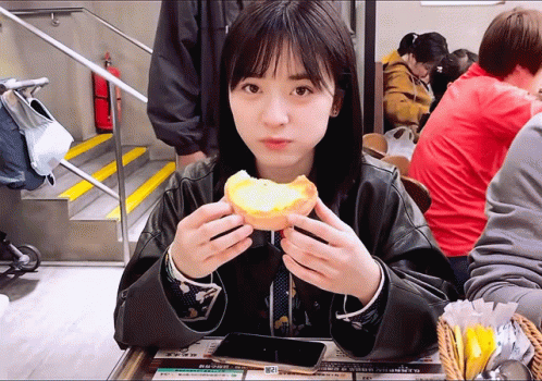 A Woman Sitting At A Table Eating A Sandwich With A Sign That Says ' A ' On It GIF