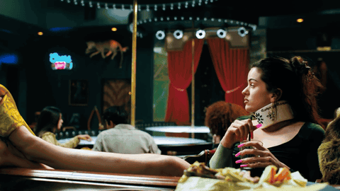 A Woman Sitting At A Table In A Bar Holding A Purse That Says ' Swag ' On It GIF