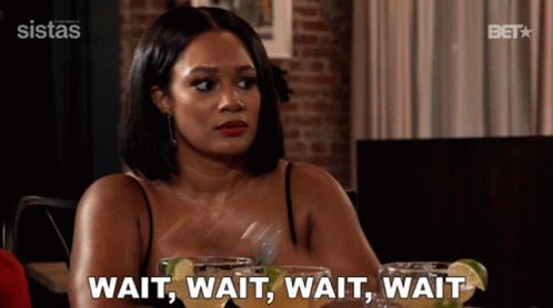 A Woman Sitting At A Table Says Wait Wait Wait Wait While Holding A Fork GIF