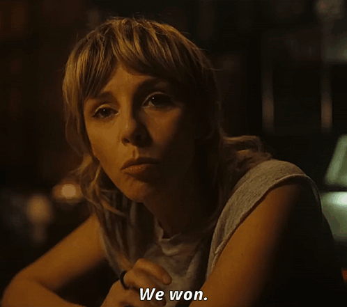 A Woman Sitting At A Table Says " We Won " In A Dark Room GIF