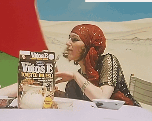 a woman sitting at a table with a box of vitos e toasted muesli in front of her