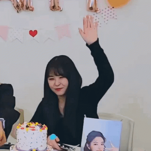 A Woman Sitting At A Table With A Cake And Balloons Behind Her With A Sign That Says " I Love You " GIF