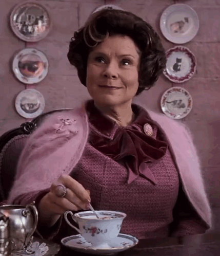 A Woman Sitting At A Table With A Cup Of Tea GIF