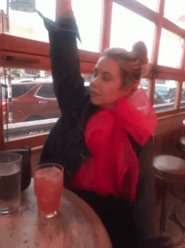 A Woman Sitting At A Table With A Glass Of Orange Liquid GIF