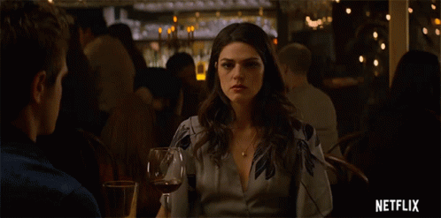 A Woman Sitting At A Table With A Glass Of Wine And A Netflix Logo GIF