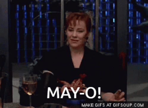 A Woman Sitting At A Table With A Glass Of Wine And The Words May-O GIF