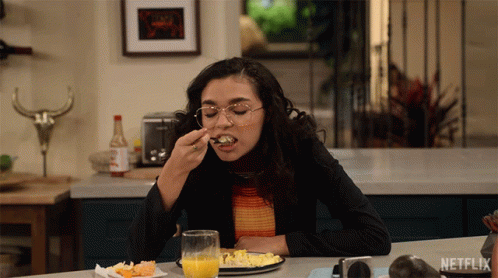 A Woman Sitting At A Table With A Plate Of Food And A Glass Of Orange Juice With Netflix Written On The Bottom GIF