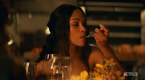 A Woman Sitting At A Table With A Spoon In Her Mouth And The Word Netflix On The Bottom Right GIF