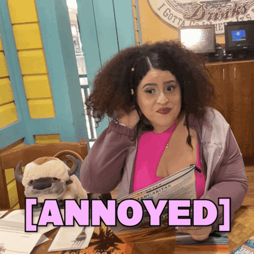 A Woman Sitting At A Table With A Stuffed Animal And The Word Annoyed On The Bottom GIF