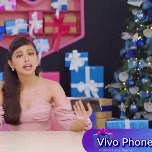 A Woman Sitting At A Table With Gifts And A Sign That Says Vivo Phone Product Link Below GIF