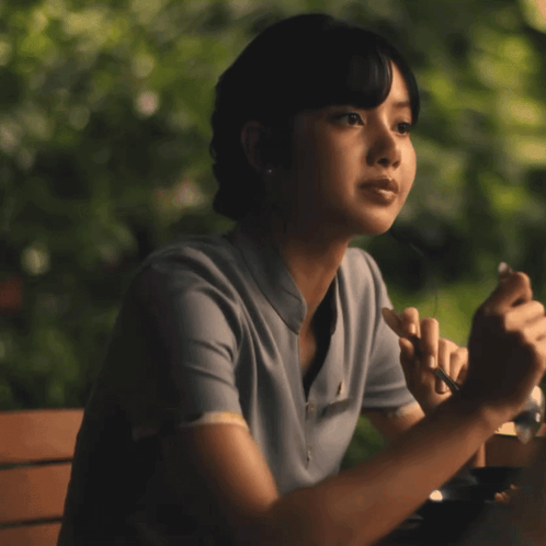 A Woman Sitting At A Table With Her Eyes Closed Holding A Pen GIF