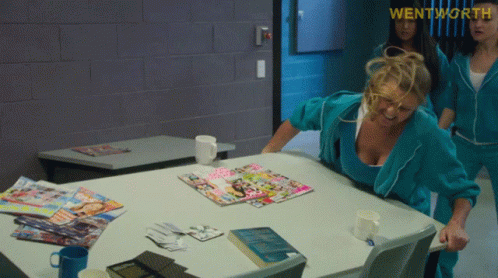 A Woman Sitting At A Table With Magazines On It And The Word Wentworth On The Bottom GIF