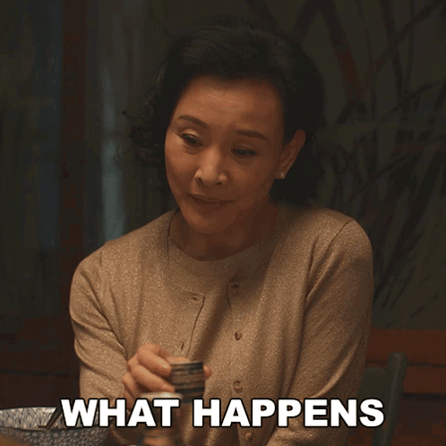 A Woman Sitting At A Table With The Words " What Happens " On Her Chest GIF