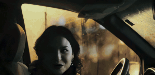 A Woman Sitting In A Car Looking Out The Window At The Camera GIF