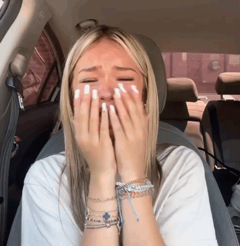 A Woman Sitting In A Car With Her Hands On Her Face GIF