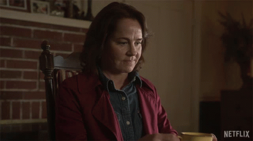 A Woman Sitting In A Chair Drinking From A Yellow Cup With Netflix Written On The Bottom GIF
