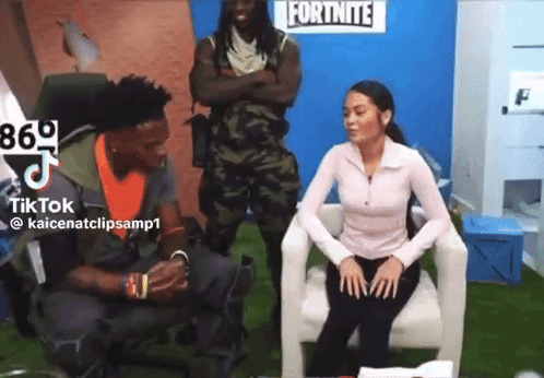A Woman Sitting In A Chair With A Man Standing Behind Her In Front Of A Fortnite Sign GIF