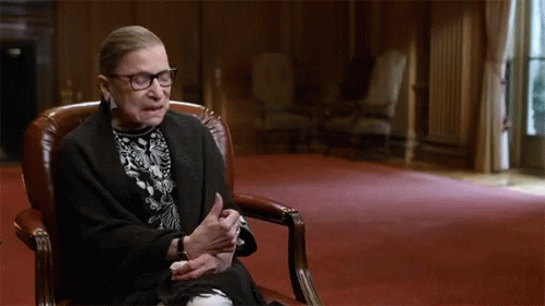 A Woman Sitting In A Chair With Her Hands Folded GIF