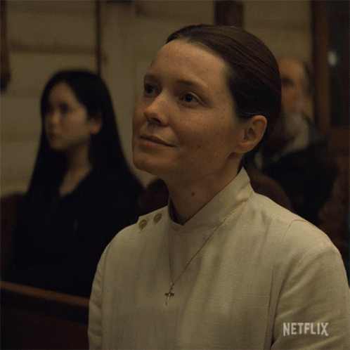 A Woman Sitting In A Church With Netflix Written On Her Sleeve GIF