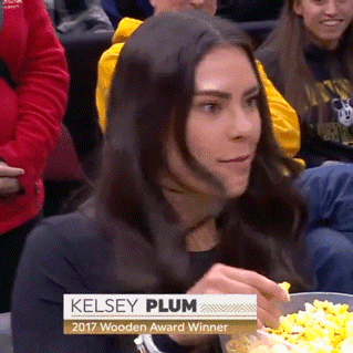 A Woman Sitting In A Crowd Eating A Bowl Of Popcorn With The Name Kelsey Plum On It GIF