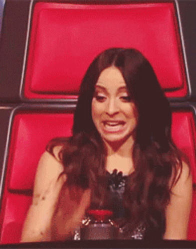 A Woman Sitting In A Red Chair Making A Face GIF