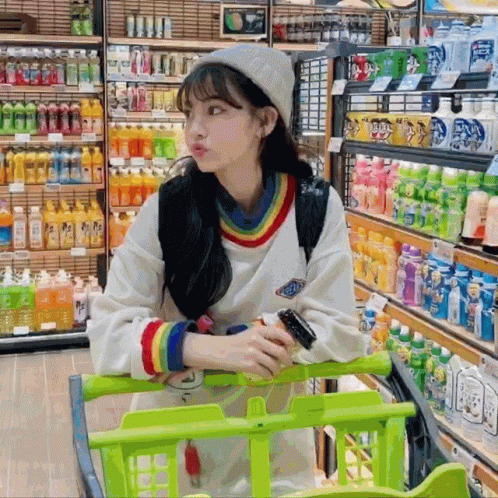 A Woman Sitting In A Shopping Cart In A Store With Bottles Of Soda On Shelves GIF