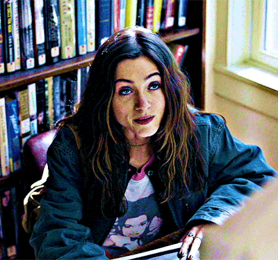 A Woman Sitting In Front Of A Bookshelf With A Book Titled ' A Brief History Of The World ' On It GIF