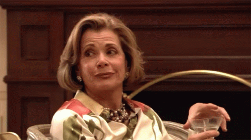 A Woman Sitting In Front Of A Fireplace Holding A Glass Of Water GIF