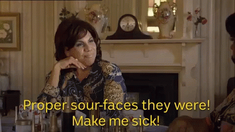 A Woman Sitting In Front Of A Fireplace With The Words Proper Sour Faces They Were Make Me Sick GIF