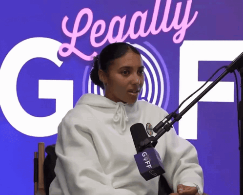 A Woman Sitting In Front Of A Microphone With A Sign Behind Her That Says ' Legally Gof ' GIF