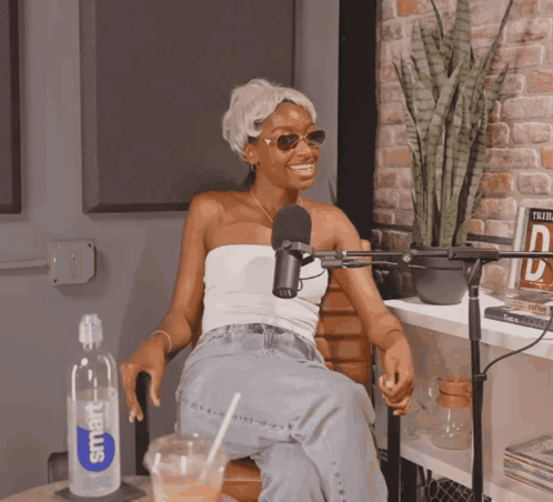 A Woman Sitting In Front Of A Microphone With A Smart Water Bottle Next To Her GIF