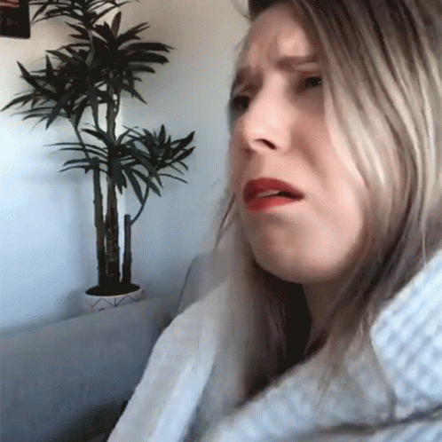 A Woman Sitting In Front Of A Potted Plant Making A Funny Face GIF