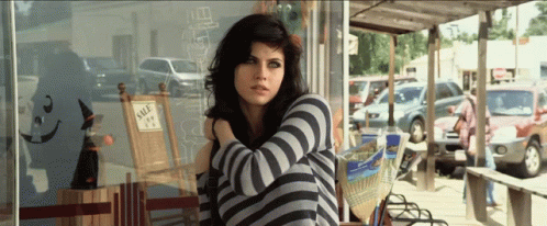 A Woman Sitting In Front Of A Store That Has A Sign That Says Sale On It GIF