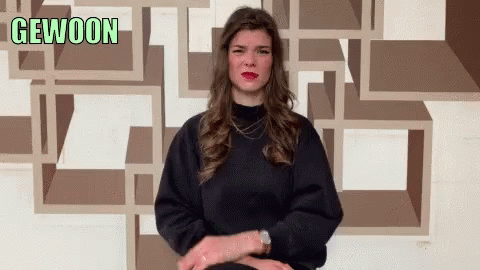 A Woman Sitting In Front Of A Wall That Says Gewoon On It GIF