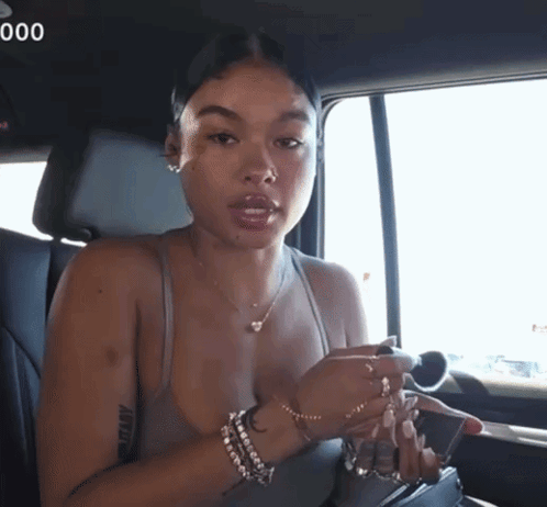 A Woman Sitting In The Back Seat Of A Car With The Number 000 On The Bottom Right GIF