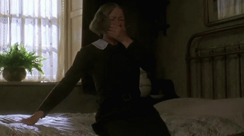 A Woman Sitting On A Bed Covering Her Mouth With Her Hands GIF