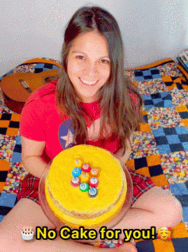 A Woman Sitting On A Bed Holding A Cake That Says " No Cake For You " On It GIF