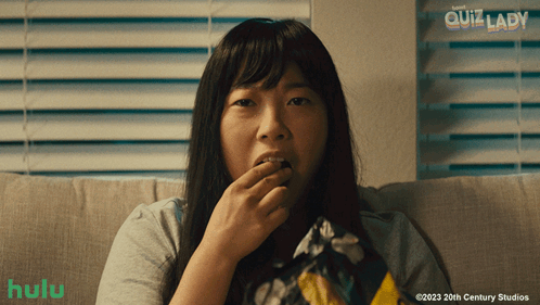 A Woman Sitting On A Couch Eating Chips With A Hulu Logo In The Corner GIF