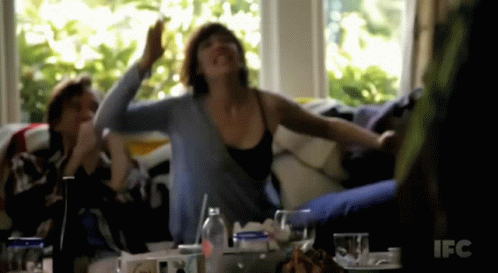 A Woman Sitting On A Couch With Her Arms Outstretched In Front Of A Ifc Sign GIF