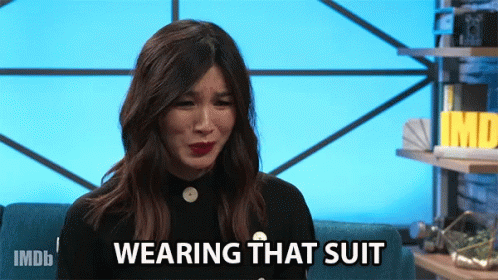 A Woman Sitting On A Couch With The Words " Wearing That Suit " On Her Face GIF
