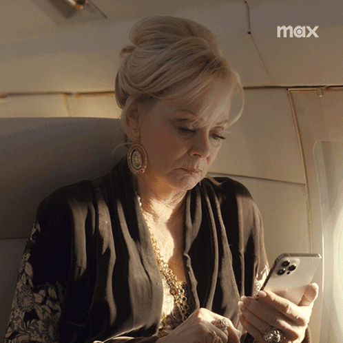 a woman sitting on an airplane looking at her phone with the max logo in the corner