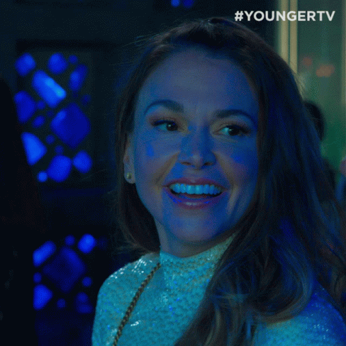 A Woman Smiles And Says " What " In Front Of A Younger Tv Logo GIF