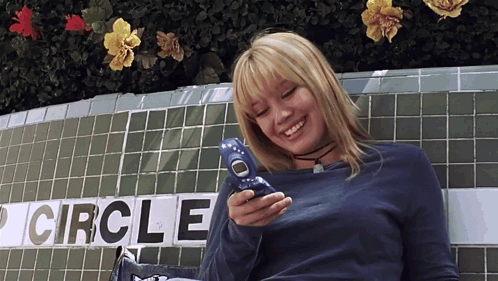 a woman smiles while holding a cell phone in front of a sign that says circle