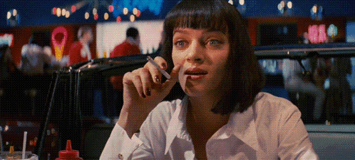 A Woman Smoking A Cigarette In A Diner With A Red Bottle Of Ketchup On The Table GIF