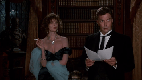 a woman smoking a cigarette next to a man reading a letter
